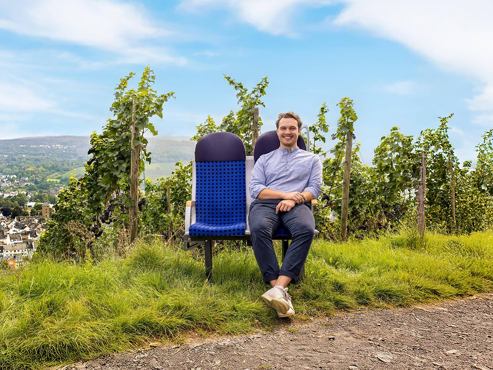 Ein junger Mann sitzt auf einer Zugsitzbank von DB Regio (vareo) mitten in den Weinbergen des Ahrtals