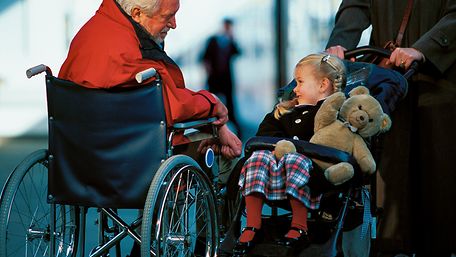 Mann im Rollstuhl neben einem Kind im Kinderwagen