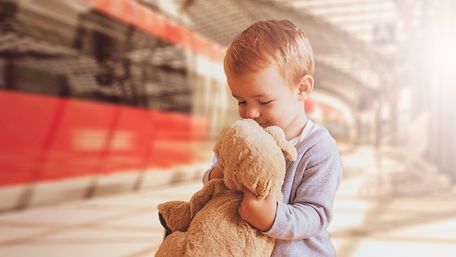 Kleinkind mit Kuscheltier am Bahnhof